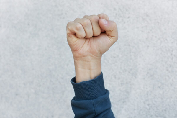 unknown person protesting, activist fist up during strike. activism for equal human rights or against racism, faceless human upraising fist isolated over white background.